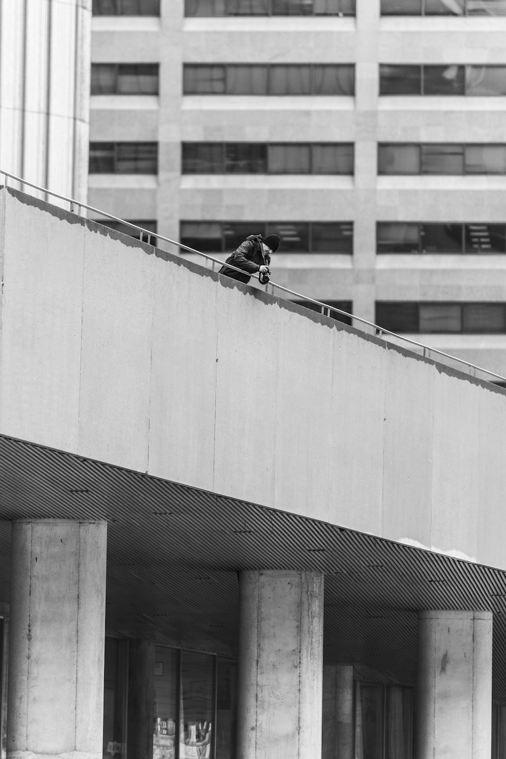 grayscaled photo of man leaning against bridge railing