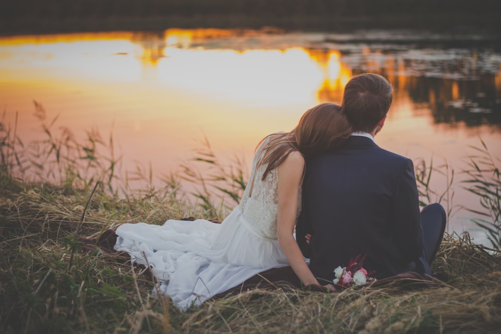 sitting woman leaning on man's shoulder facing lake during golden hour