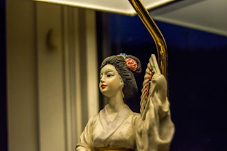 A close-up of a delicate, hand-painted figurine sitting on a wooden desk bathed in soft natural light.
