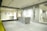An interior space featuring a modern showroom with large ceramic tiles and bright lighting. The walls display brand signage and various tile samples. A sleek, minimalist desk is centered, surrounded by a clean and spacious environment.