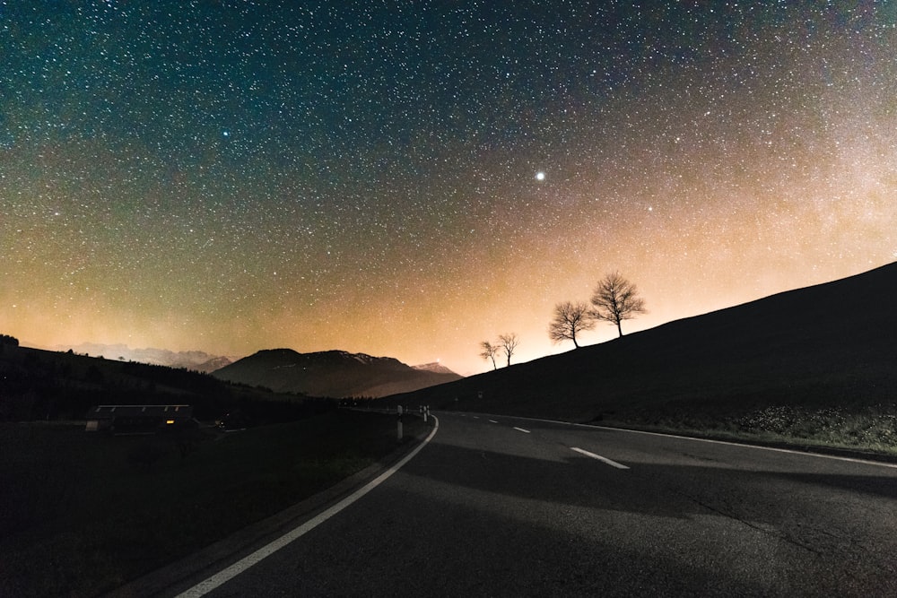 gray asphalt road near silhouette of mountain at night time
