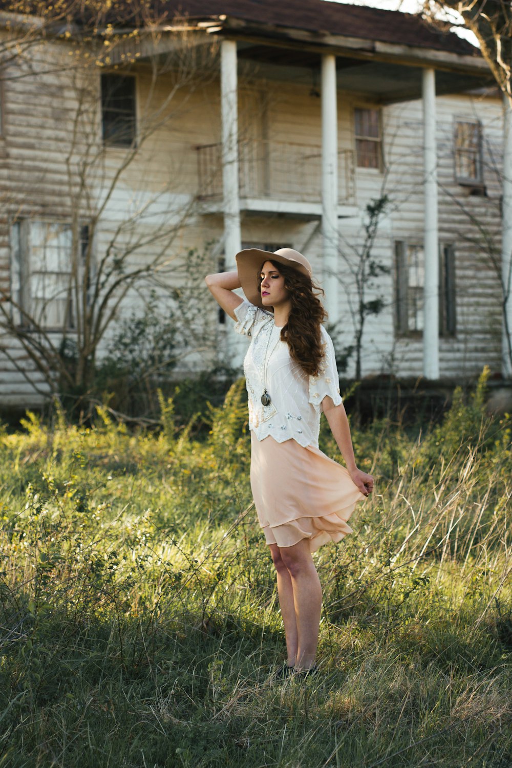 woman wearing brown sun hat standing on grass near white house