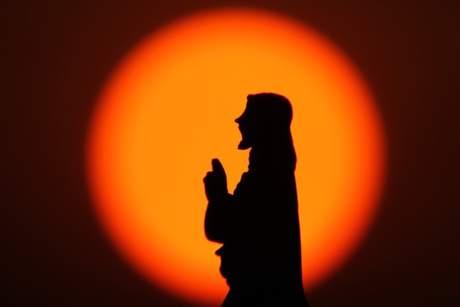Hands joined in prayer with a backdrop of a warm, glowing sunset.