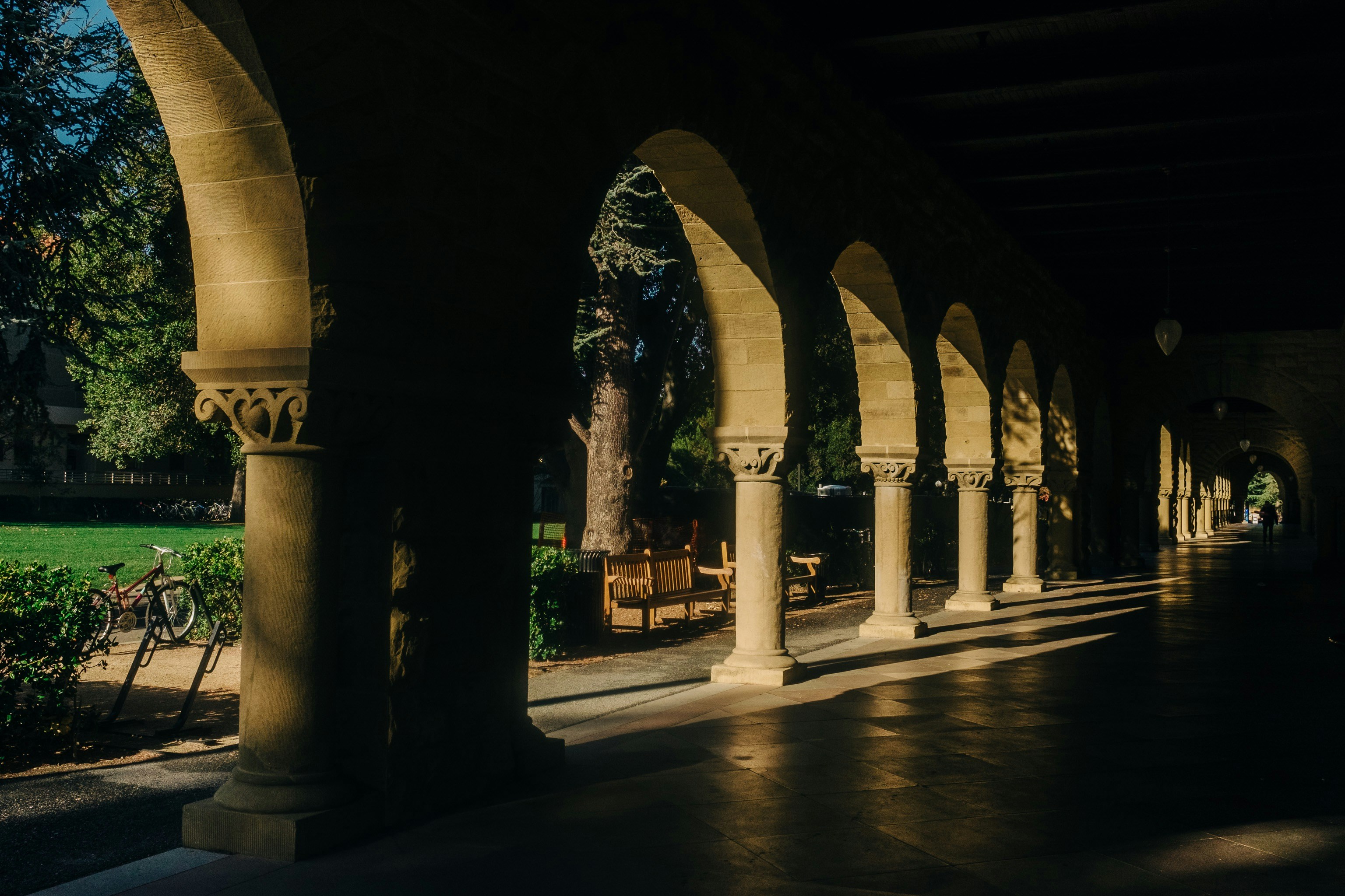 an iconic columned arcade at Stanford university with lawn and trees and bicycles visible through openings