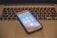 A smartphone displaying a call screen rests on the keyboard of a laptop. The laptop keyboard is slightly out of focus, and the smartphone shows an ongoing call with several icons for call options.