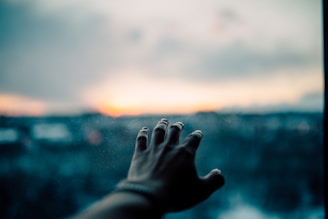 A hand reaching towards a blurred landscape with a sunset in the background creates a sense of longing and distance.