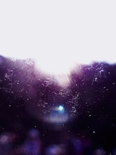 Bright light with lens flares against a dark background, creating a cosmic or ethereal effect. Light particles and dust are scattered throughout the scene.