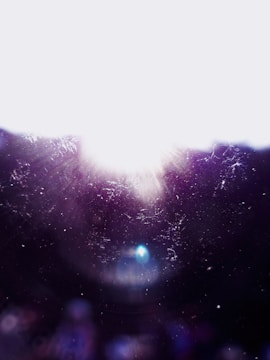 Bright light with lens flares against a dark background, creating a cosmic or ethereal effect. Light particles and dust are scattered throughout the scene.