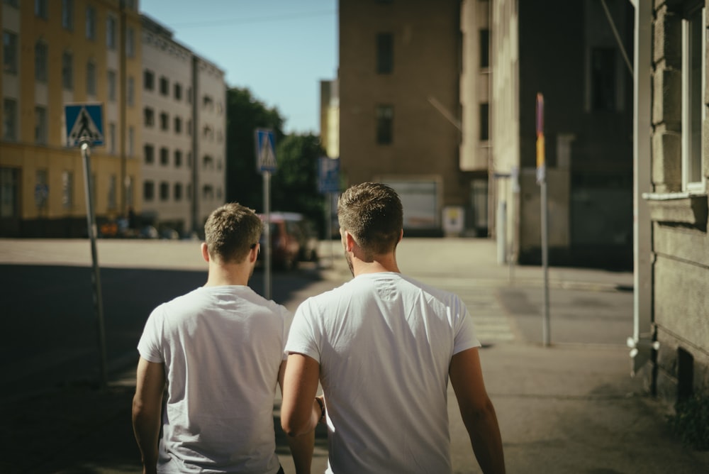 Two men in white t-shirts walk away down a city street