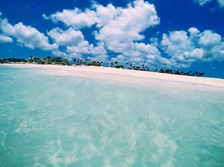A sunlit beach with crystal-clear water and a cozy resort in the background.