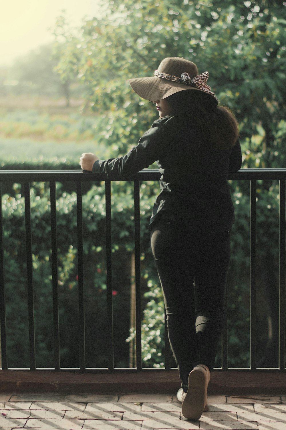 woman in black jacket and black pants wearing brown hat standing beside black metal fence during