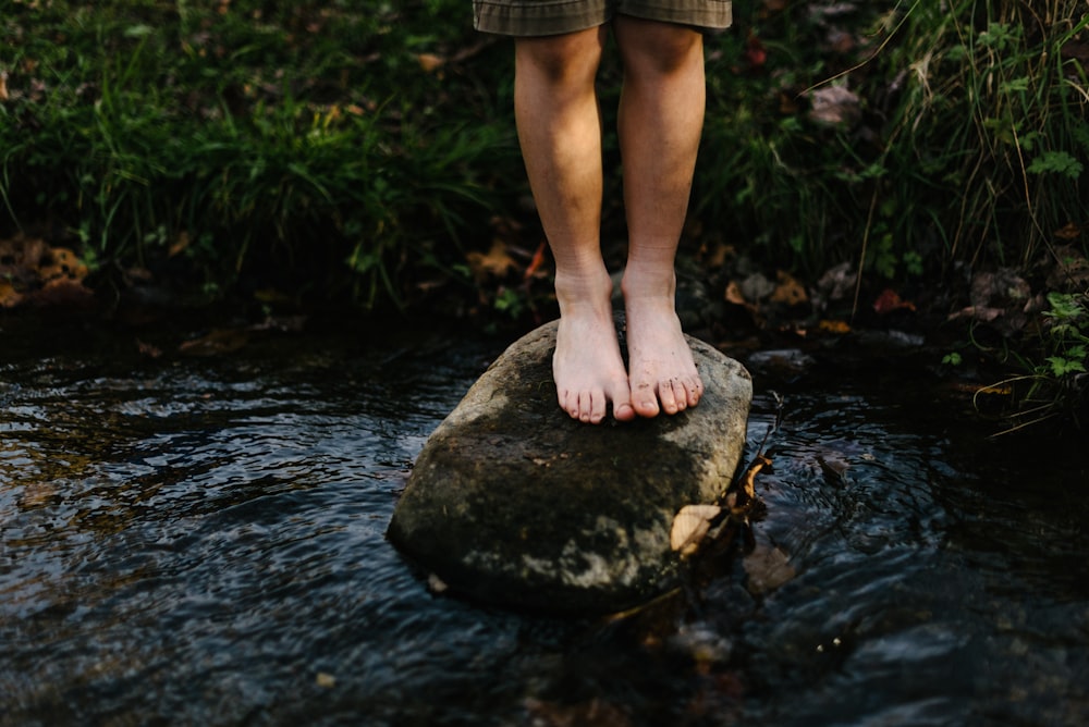 person standing on stone at center of body of water