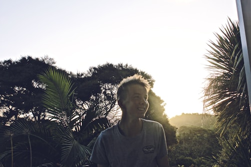 Justin Canelas smiling warmly in a lush Kaʻū farm setting, embodying his connection to the land and community.