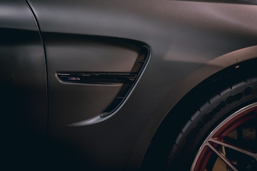 A detailed image of the side vent and wheel of a high-performance car, emphasizing the smooth matte finish of the vehicle's body and the intricate design of the alloy wheel with red detailing.