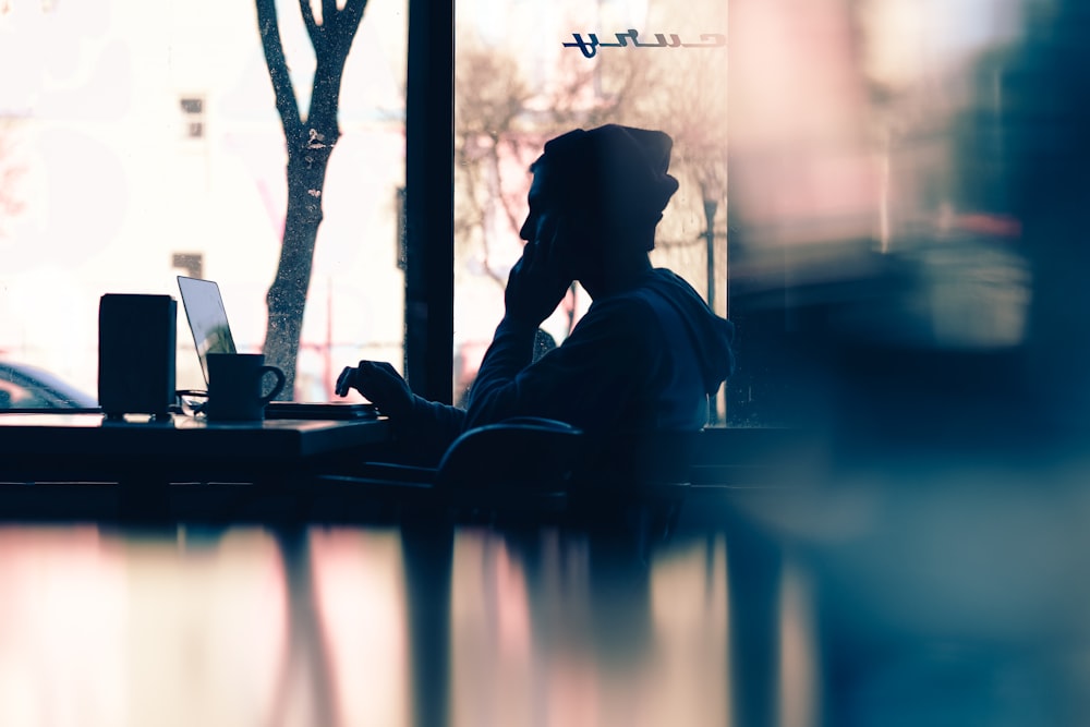 silhouette of a person sitting in front of a laptop