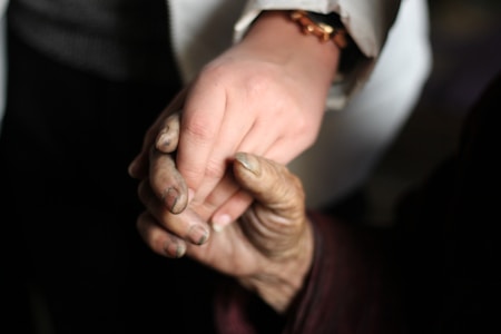 A young, clean hand gently holds an older, weathered hand, highlighting the contrast between the smooth, soft skin and the rough, aged appearance.