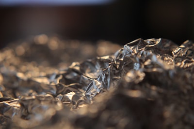 Crumpled silver foil with intricate patterns and reflections catches the light, creating a textured and shiny surface.