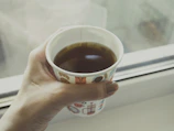A candid photo of hands holding a steaming cup of coffee by a window
