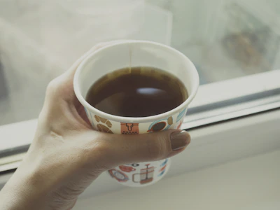 A candid photo of hands holding a steaming cup of coffee by a window