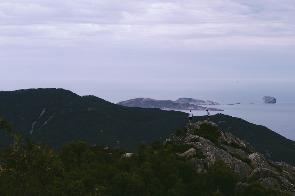 two men standing at top of mountain near sea