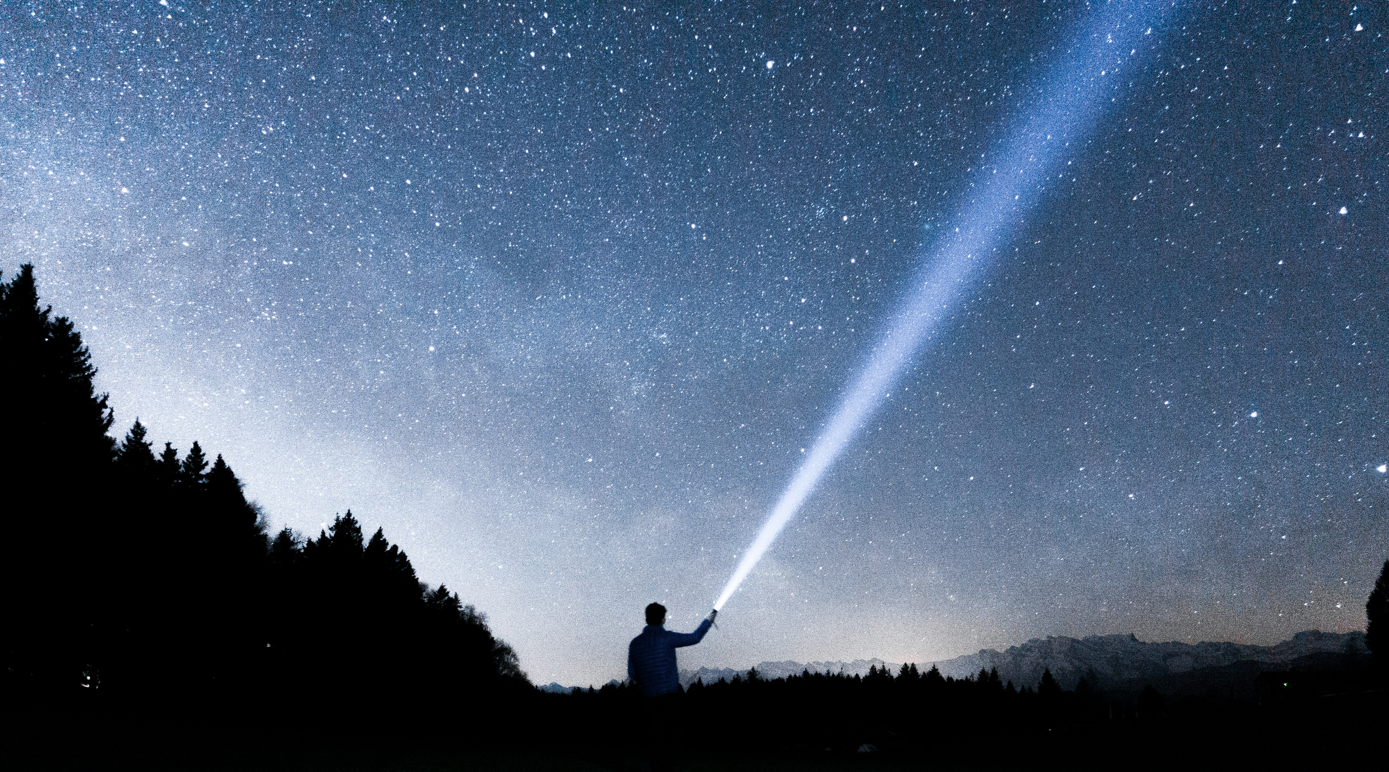 silhouette of person holding flashlight during nighttime