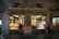 A historic storefront with elegant architectural details houses an interior filled with beautifully displayed products. The windows are warmly lit, showcasing various confectionery items inside. A person is visible inside admiring the displays, while another person walks by outside. The signage above the store reads 'Pietro Romanengo fu Stefano.'
