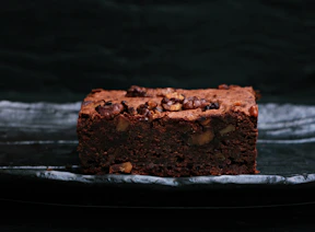 Brownies with nuts and caramel swirls on a dark chocolate background.