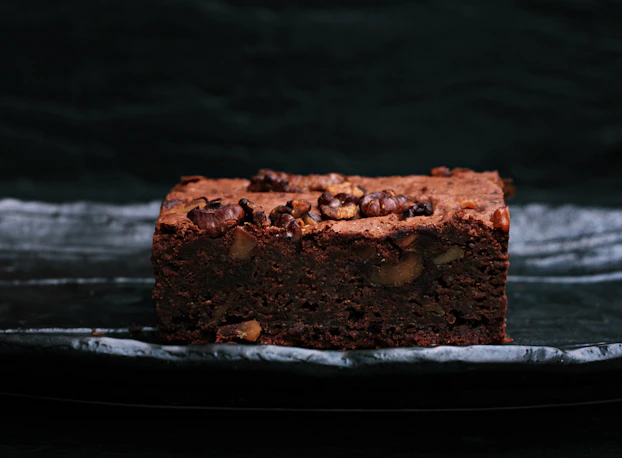 Brownies with nuts and caramel swirls on a dark chocolate background.
