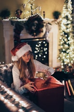 woman putting ribbon in red gift box near lighted Christmas tree inside room