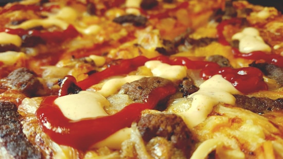 A close-up of a pizza topped with melted cheese, slices of sausage, and a generous amount of ketchup and mayonnaise drizzled on top.