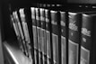 A row of hardcover books lined up on a shelf, featuring prominently displayed titles and authors on their spines. The image is captured in black and white, giving it a classic and timeless feel.