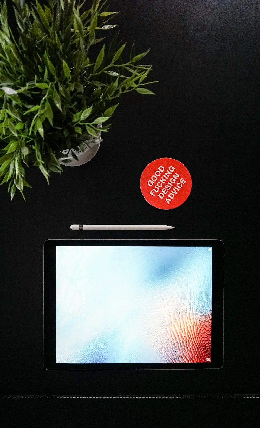 black iPad next to Apple pen near green leaf plant