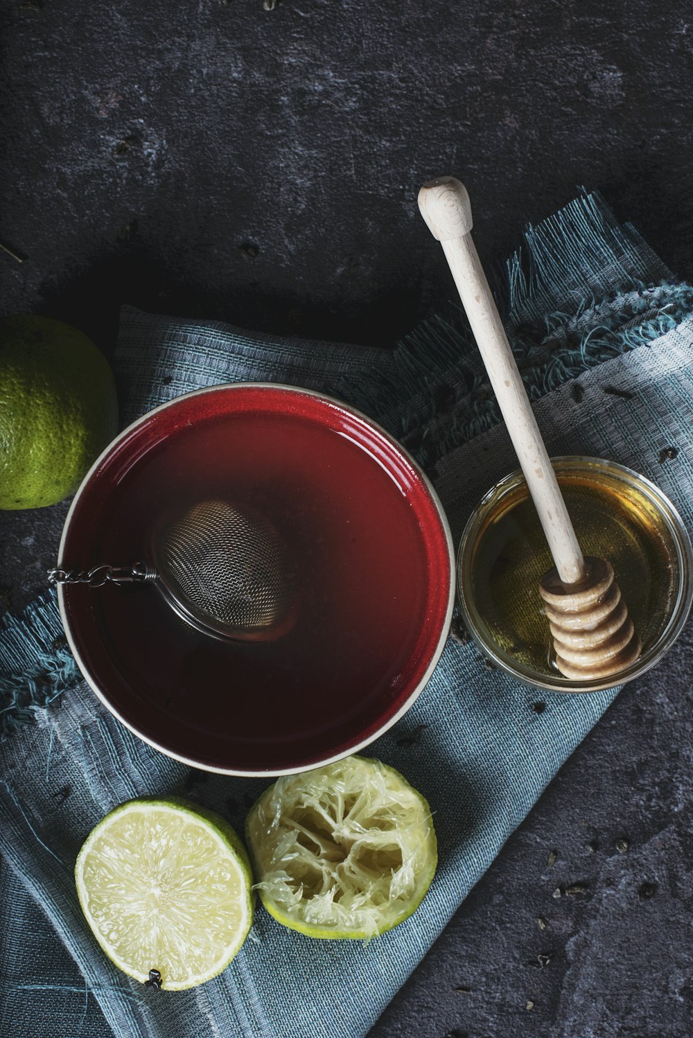 Bol en céramique rouge rempli d’eau à côté de citron vert et de miel