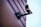 A security camera mounted on a wall with visible cables. The wall has a textured surface with horizontal lines, and the background is a clear blue sky.
