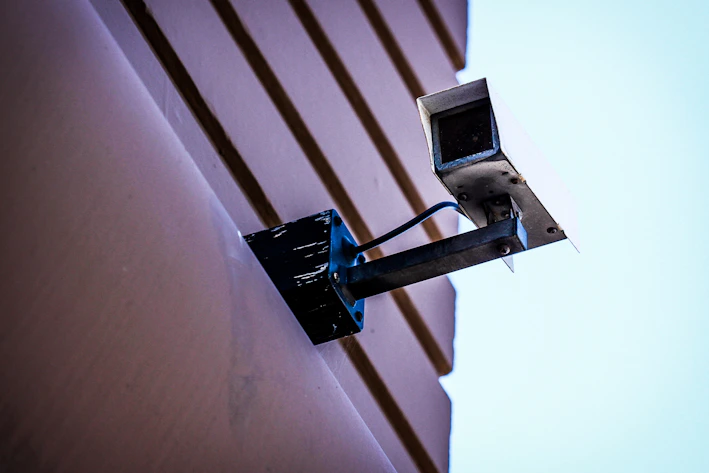 A sleek modern security camera mounted on a wall with a clear blue sky background