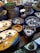 A collection of colorful, intricately designed ceramic dishware featuring artistic patterns and illustrations. The items include plates and bowls with vibrant hues of blue, yellow, and white, and illustrations depicting traditional scenes.