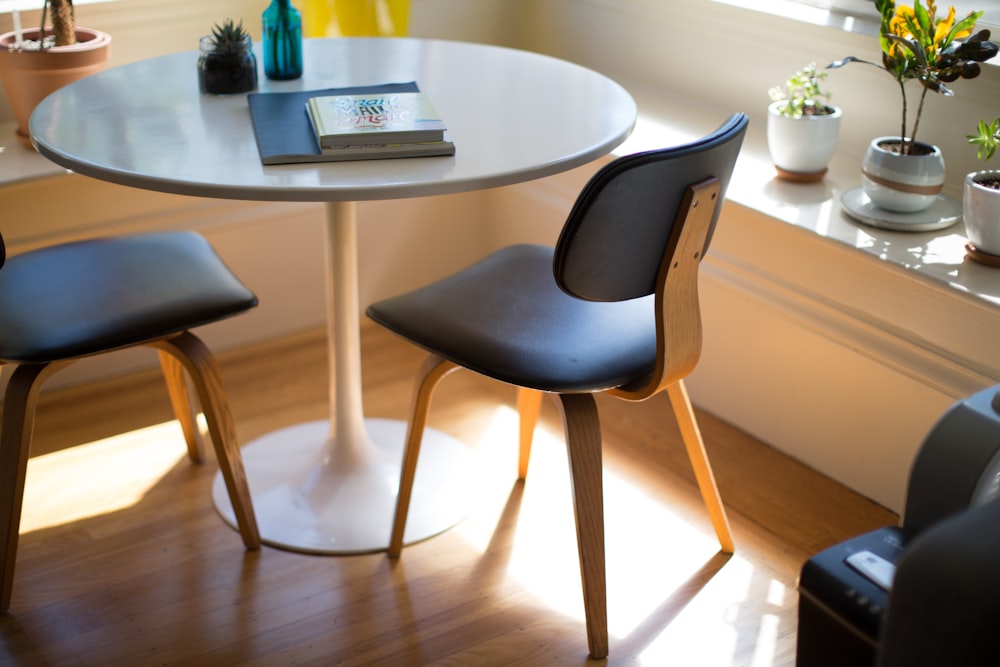 Mesa de comedor blanca redonda junto a dos sillas sobre suelo de madera marrón