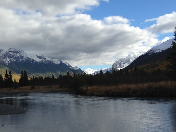 A peaceful river winding through a valley with snow-capped mountains in the distance.