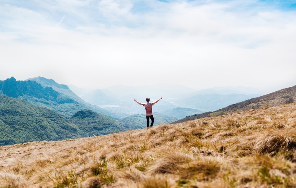 man topless standing on top of hill with dried grass field