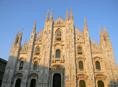 A sunlit view of the intricate gothic spires and statues atop the Duomo di Milano against a clear blue sky.