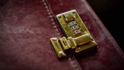 A close-up of a polished gold combination lock attached to a distressed, dark red leather surface, likely part of a briefcase or similar item.