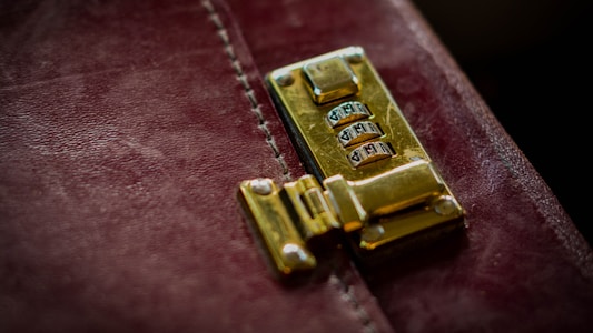 A close-up of a polished gold combination lock attached to a distressed, dark red leather surface, likely part of a briefcase or similar item.