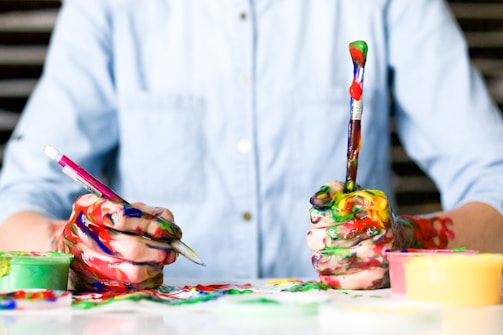 Hands creating art with paintbrushes and vibrant paints.