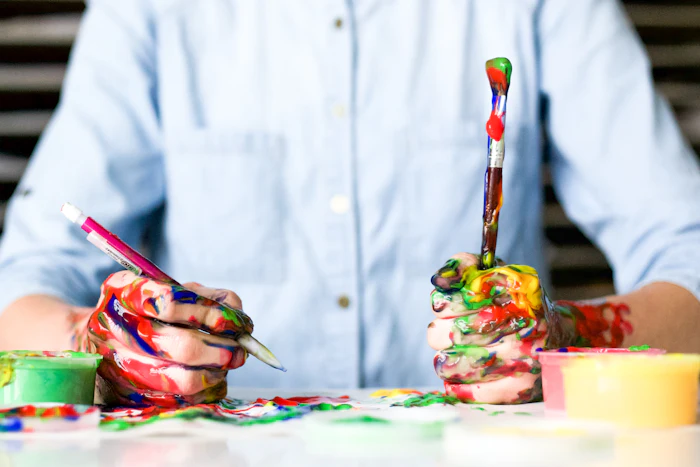 Hands covered in paint, mid-project, brushes in the air