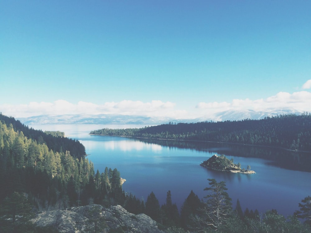 Lago circondato da montagne e alberi sotto il cielo blu