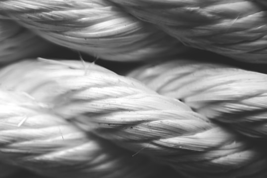 A close-up view of a thick, twisted rope with visible fibers and texture. The image appears to be in black and white, showcasing the intricate details and interwoven strands of the rope material.