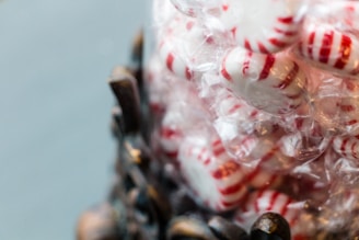 A pile of peppermint candies with red and white stripes is wrapped in clear plastic. The candies are stacked upon one another, creating a sense of abundance and sweetness.
