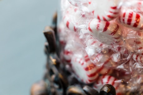 A pile of peppermint candies with red and white stripes is wrapped in clear plastic. The candies are stacked upon one another, creating a sense of abundance and sweetness.