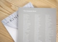 Two books are placed on a light wooden surface. The top book is titled 'The Unsplash Book' and features a list of names printed in white on a light gray cover. Part of the title 'THE KIN' is visible on the book underneath, with a partially visible white cover and black text.