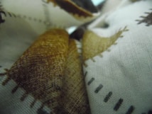 Fabrics displayed with a close-up view of a textured surface, featuring patterns with brown and black stitching against a white background. The material appears to be layered, creating a sense of depth.